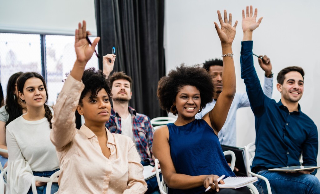 university students in classroom raising their hands