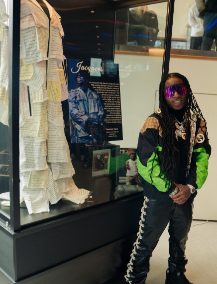 Singer Jacquees standing beside a glass display case featuring his performance costume