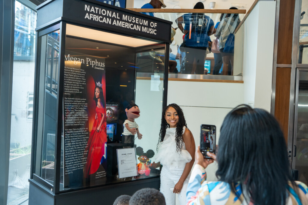 Megan Piphus posing in front on glass exhibition case containing puppets and display